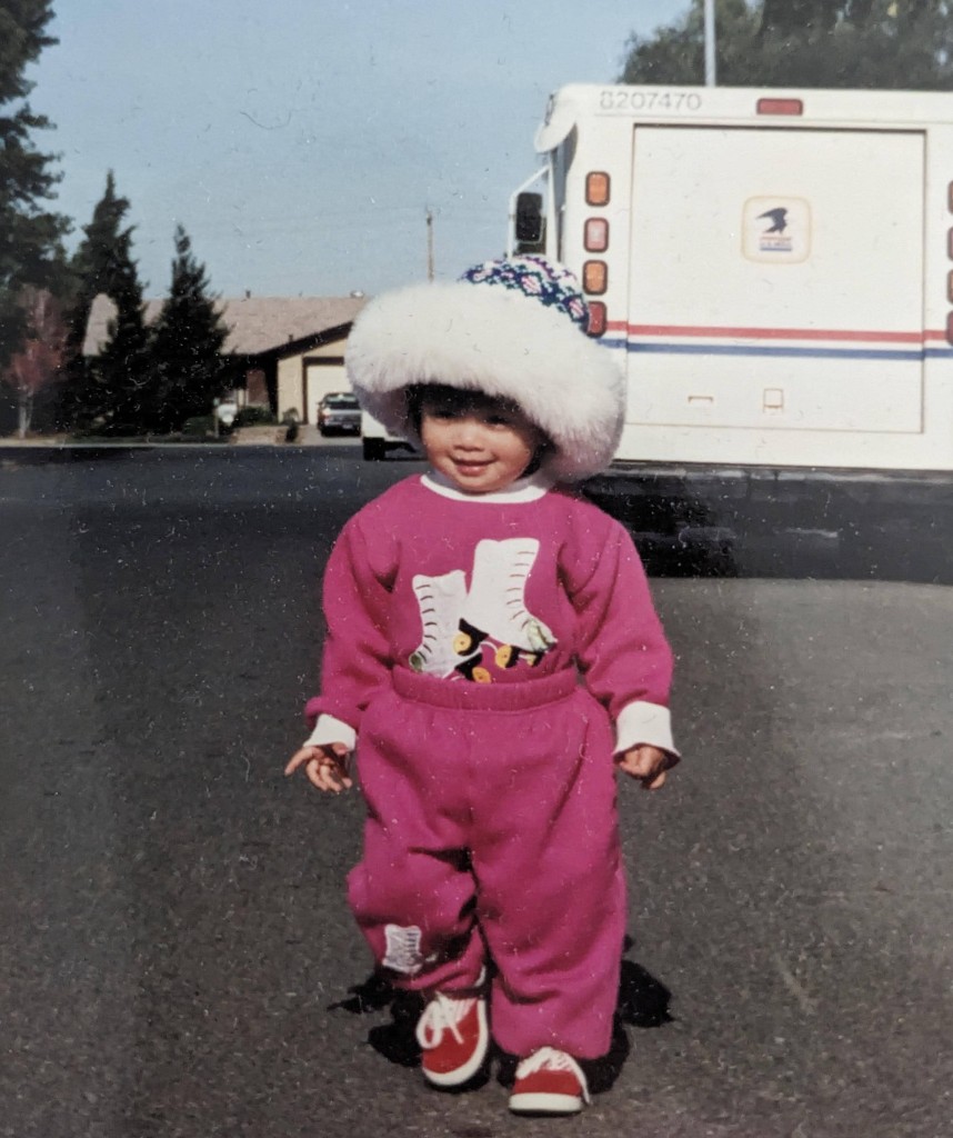Young Trang standing outdoors in a pink sweatsuit and white hat.